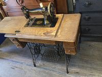 Full view of antique Singer sewing machine mounted on wooden cabinet showing the sewing machine surface with delicate gold detailing.