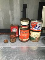 Full view of 7 varying vintage automotive tins showing paint wear and rust spots, arranged on a metal surface.