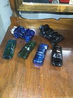 Six collectible glass cars in various colors on a wooden surface showing details and color variation.