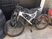 Full side view of the Supercycle Thrill mountain bike leaning against a wall with spare tires in the background.