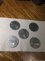 Five Canadian silver dollar coins laid out on a cloth, showing the reverse side with the Voyageur canoe design and dates.