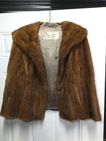 Full front view of the vintage brown fur coat on a hanger.
