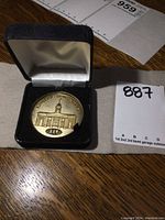 Photo showing the coin inside a black, hinged fitted display case with satin inside lid and velvet cushion with coin resting on top.