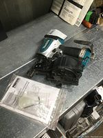 Makita pneumatic coil roofing nailer with manual and oiler accessory on a metal surface.