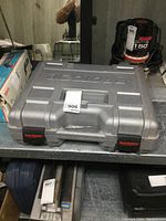 Closed gray hard plastic carrying case with Rotozip branding embossed on lid, placed in storage area with other tools visible around.