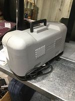 Gray hard plastic carrying case with handle for Ryobi biscuit joiner, placed on a table.