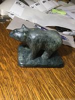 Side angle view of greenish-grey soapstone bear sculpture on wood table with signed base and original price tag.