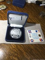 Silver commemorative coin in protective case with certificate of authenticity visible, showing $75 price tag.