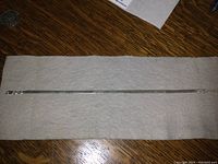 Full length of silver herringbone bracelet laid flat on fabric background.