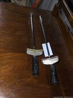 Pair of two vintage Hastings torque wrenches laid on a wooden table, showing full length and handles.