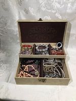 Top-down view of the open jewelry box showing compartments filled with assorted jewelry and a purple fabric lining in the lid with a decorative design