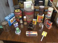 Full view of vintage kitchen collectibles on wooden surface with a mirror behind, showing various tins, boxes, bottles, and kitchen tools.
