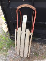 Front view of vintage wood and metal sleigh showing wooden seat slats, metal frame and handle with wooden grip.