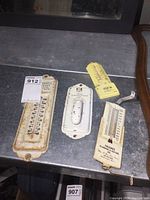 Photo showing three vintage metal thermometers and one metal paper holder placed on a table.