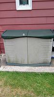 Front view of Rubbermaid backyard storage bin showing twin lids and locking mechanism, some dirt on front.