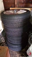 Stack of four tires with rims against garage wall.