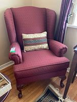 Front view of red patterned fabric armchair with wooden legs and decorative cushion on seat.