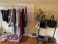 Full view of two clothing racks side by side against wall, one with black plastic base and other with metal base, both with clothes and bags (not included).