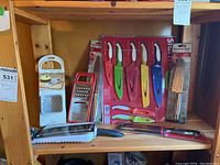 Shelf with various new kitchen cutting utensils including colorful Starfrit knife set and two graters.