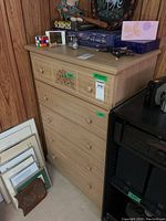 Front and side view of the laminate wood dresser with five drawers, showing a decorative floral detail on the top drawer and wooden knob handles.