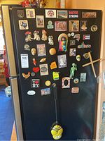 Fridge front covered with assorted fridge magnets from various themes including travel destinations, animals, and novelty designs.