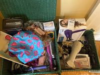 Various hair care and styling tools in a green basket including boxed Conair hair dryer, curling irons, brush, hair clips and scrunchies.