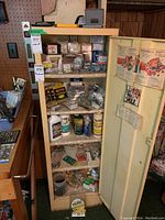 Full view of upright metal cabinet filled with assorted hardware items including screws, staples, casters, lubricants, and cleaning products.
