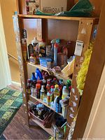 Wooden shelving with assorted household cleaning products including liquids, sprays, aerosols, brushes, and cleaning accessories.