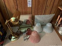 Photo of brass desk lamp, vintage glass lamp shades, and rectangular framed mirror arranged on beige carpet against wood-paneled wall.