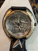 Front close up of watch face showing detailed USS Enterprise and Star Trek logo with stamped minute markers.