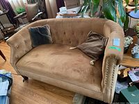 Front and angled view of light brown velvet loveseat with two cushions, showing tufted backrest and stud detailing on arms and base.