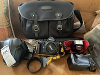 Full kit arranged on surface including camera body with lens and strap, lens hood, charger, flash unit, case and bag