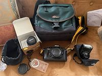 Wide view of all items: camera body, lens, flash, bag, caps, pouch and compass