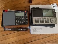 Overview of Sangean ATS-909X2 and Tecsun PL-880 with their boxes and cases on wood floor