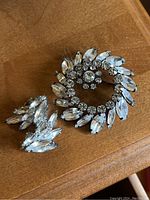 Photo of Sherman rhinestone brooch and clip-on earrings on wooden surface showing clear rhinestones in silver-tone setting