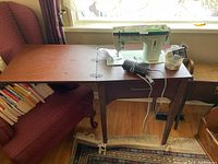 Wooden sewing machine cabinet with sewing machine mounted on top and accessories beside it.