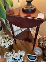 Front angled view of the dark wood triangular side table showing the three drop-down leaf tabletop and lower corner shelf with decorative legs.