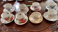 Set of eight teacups with matching saucers placed on wooden table showing floral and gold accent details.
