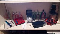 Shelf with electronics tools including Micronta multimeter, pliers, screwdriver set, soldering iron, wire spools and coiled test leads.
