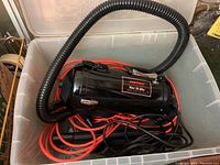 Top view of Metro Vac 'N Blo vacuum/blower unit, black cylinder shape with hose and cords inside a clear plastic storage bin.