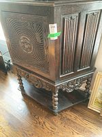 Front side angle of antique wooden cabinet showing caned door with decorative medallion and carved detailing on the legs and apron.