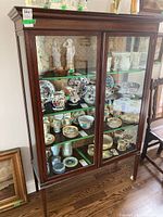 Full front view of the antique glass doored display cabinet filled with various ceramic collectibles.