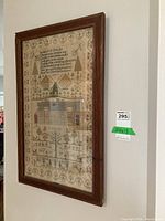 Full view of framed sampler hanging on wall in wood frame.