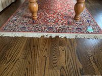 Photo of the area rug showing the detailed fringe damage and the section under furniture legs on hardwood floor.