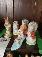 Group photo of 5 porcelain Beatrix Potter character figurines including squirrel, mouse in red jacket, rabbit with basket, girl in blue dress, and mouse in boat.