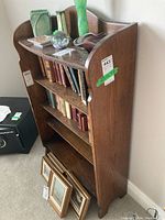 Full perspective view of wooden bookcase showing side panel curved design, three shelves filled with books and decorative items on top.