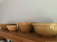 Side view of the five yellowish-brown glazed bowls lined up from large to small showing size variation and surface patterns.