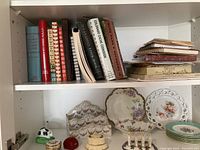 Shelf with assorted cookbooks, vintage binding, and spiral notebooks.