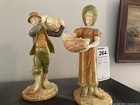 Front view of both porcelain figurines, boy and girl carrying baskets