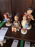 Four Goebel Hummel figurines displayed on a wooden surface showing overall view of the lot.